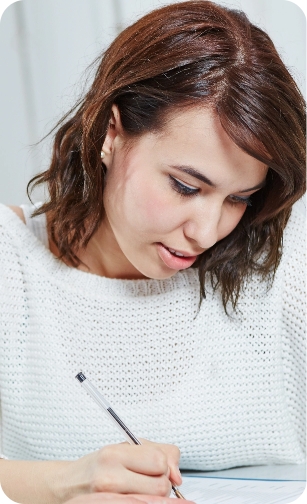 Newcastle Specialist Prosthodontics Young woman in a white sweater writing on paper while looking down.